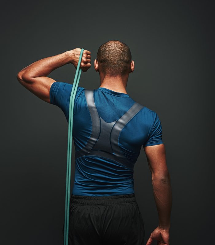 Give your best. Sportsman standing with resistance band over dark background. Back view